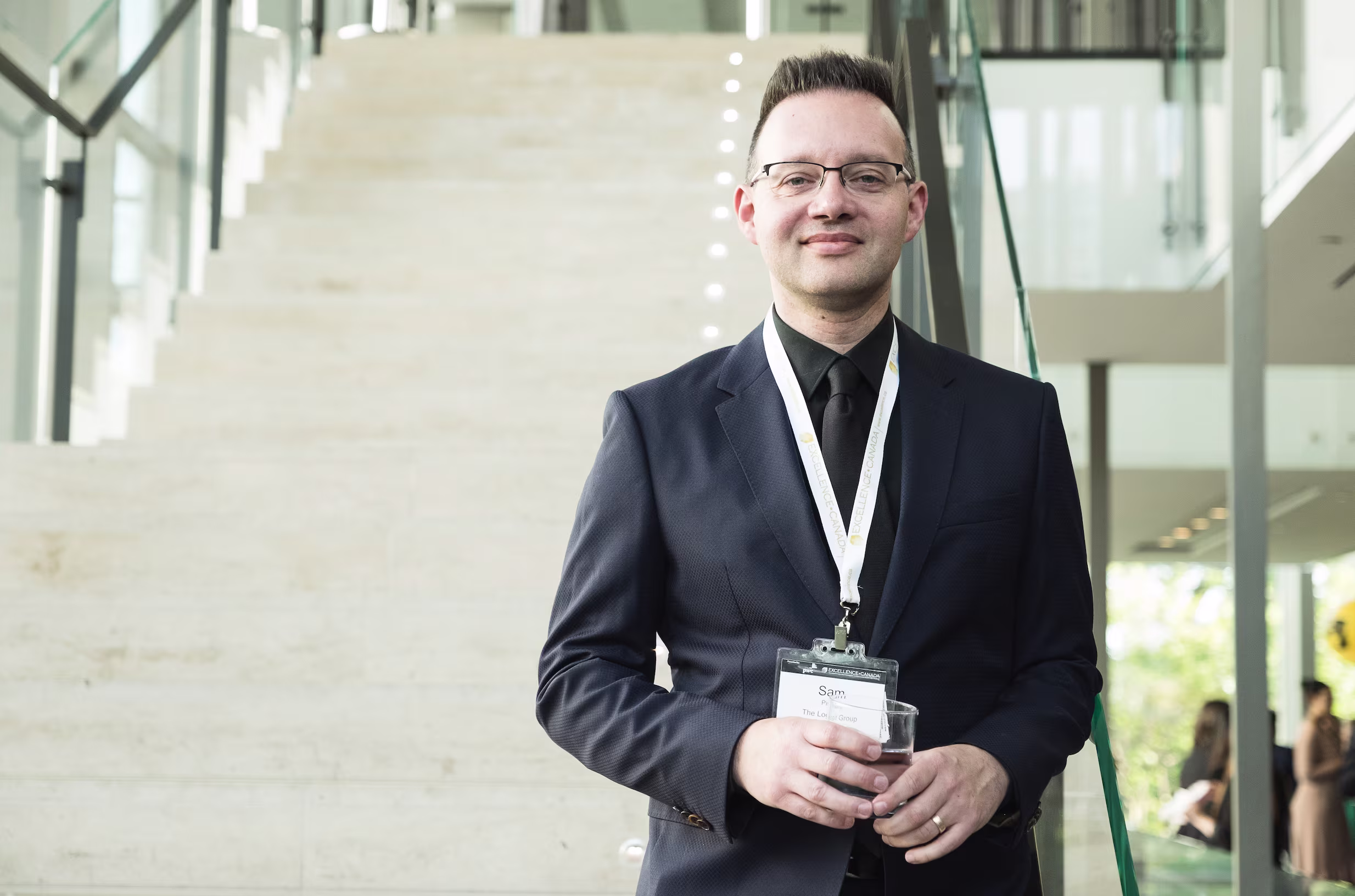 Man wearing a suit and event badge posing for a portrait inside a modern venue.
