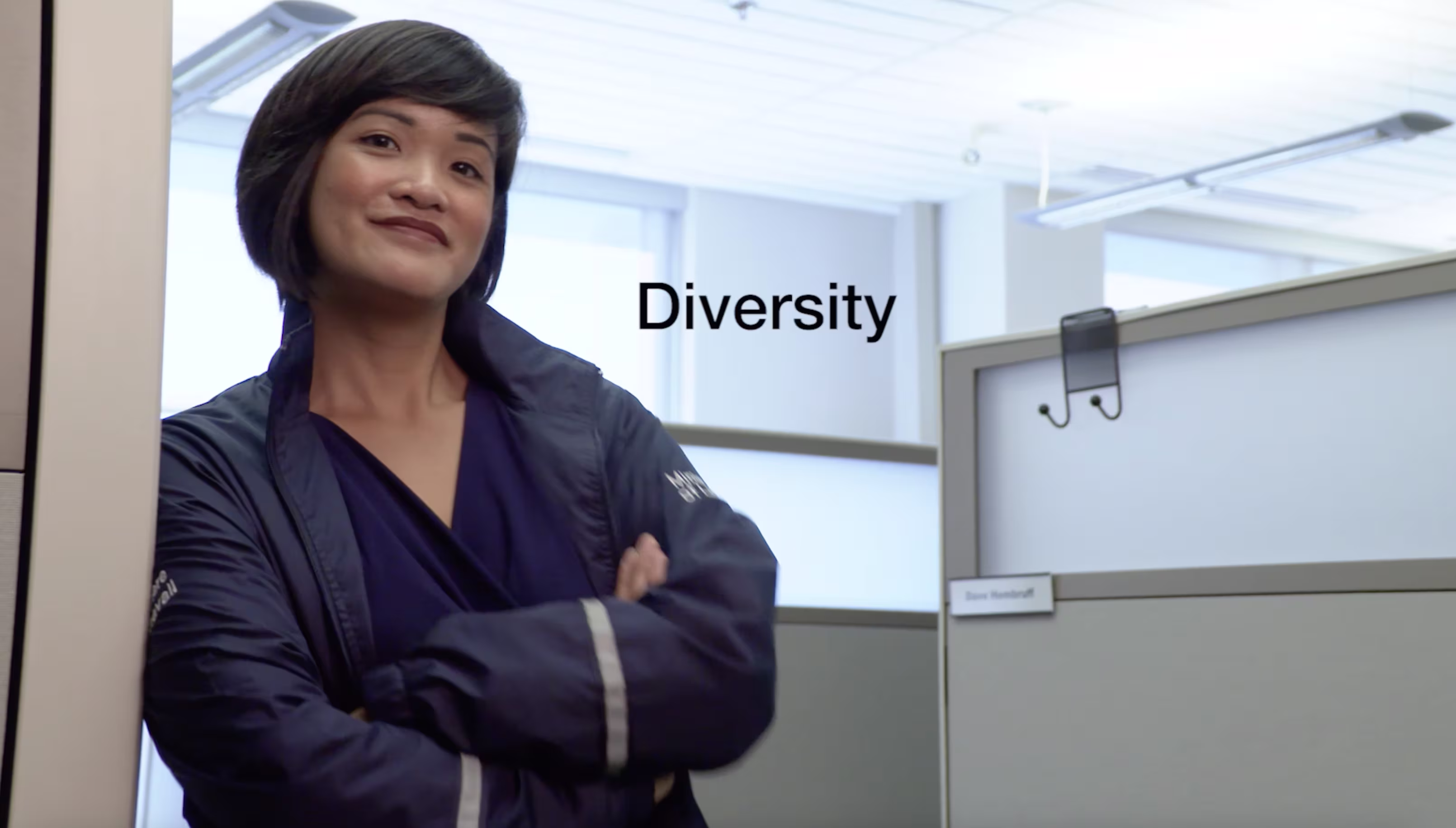 Woman standing confidently in an office cubicle area with arms crossed.