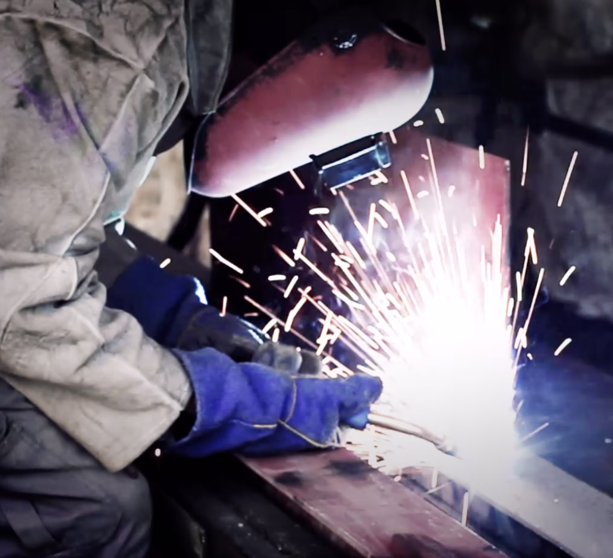 Close-up of a worker welding metal with bright sparks flying in an industrial setting.
