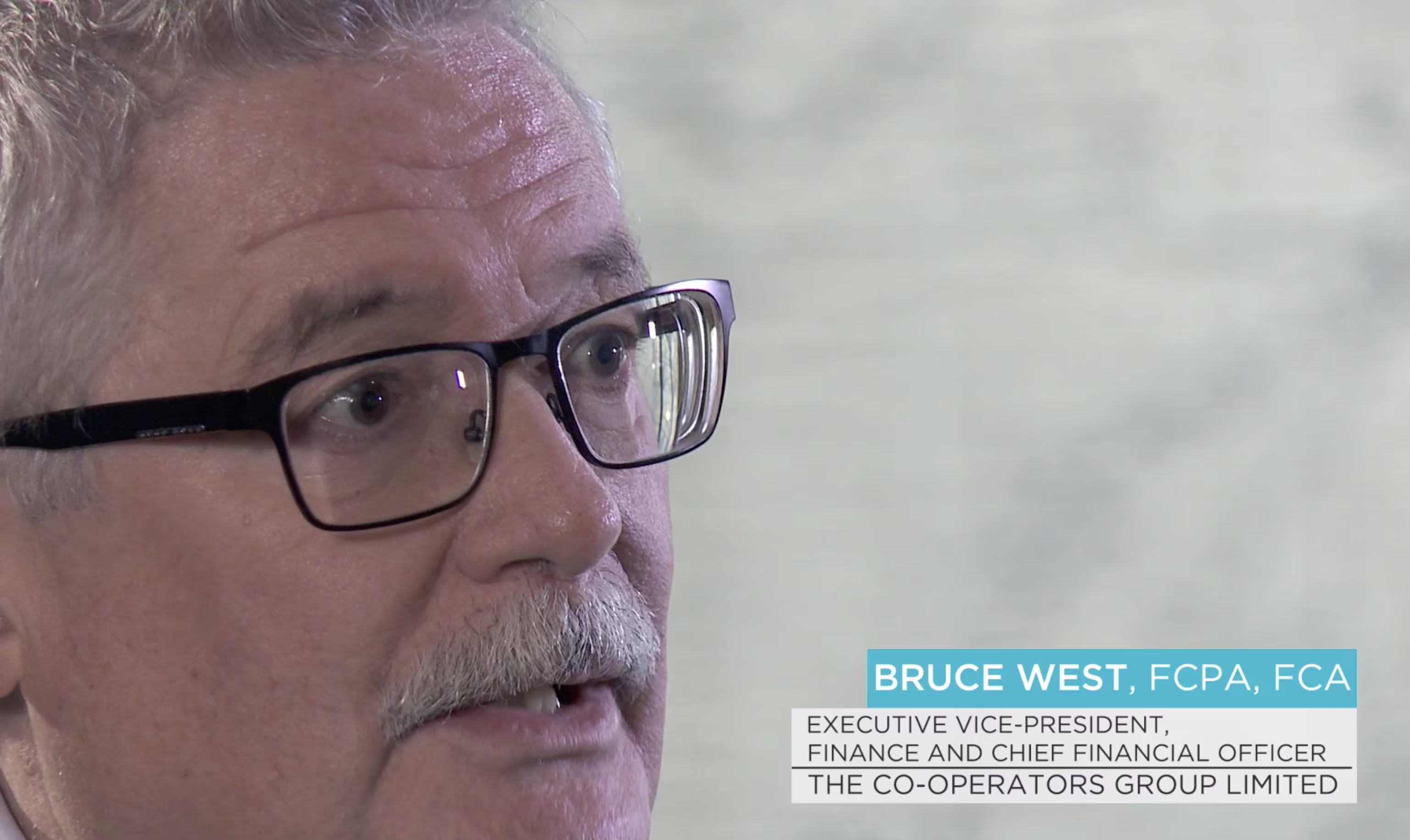 Close-up of a man wearing glasses speaking during an interview, identified as Bruce West.