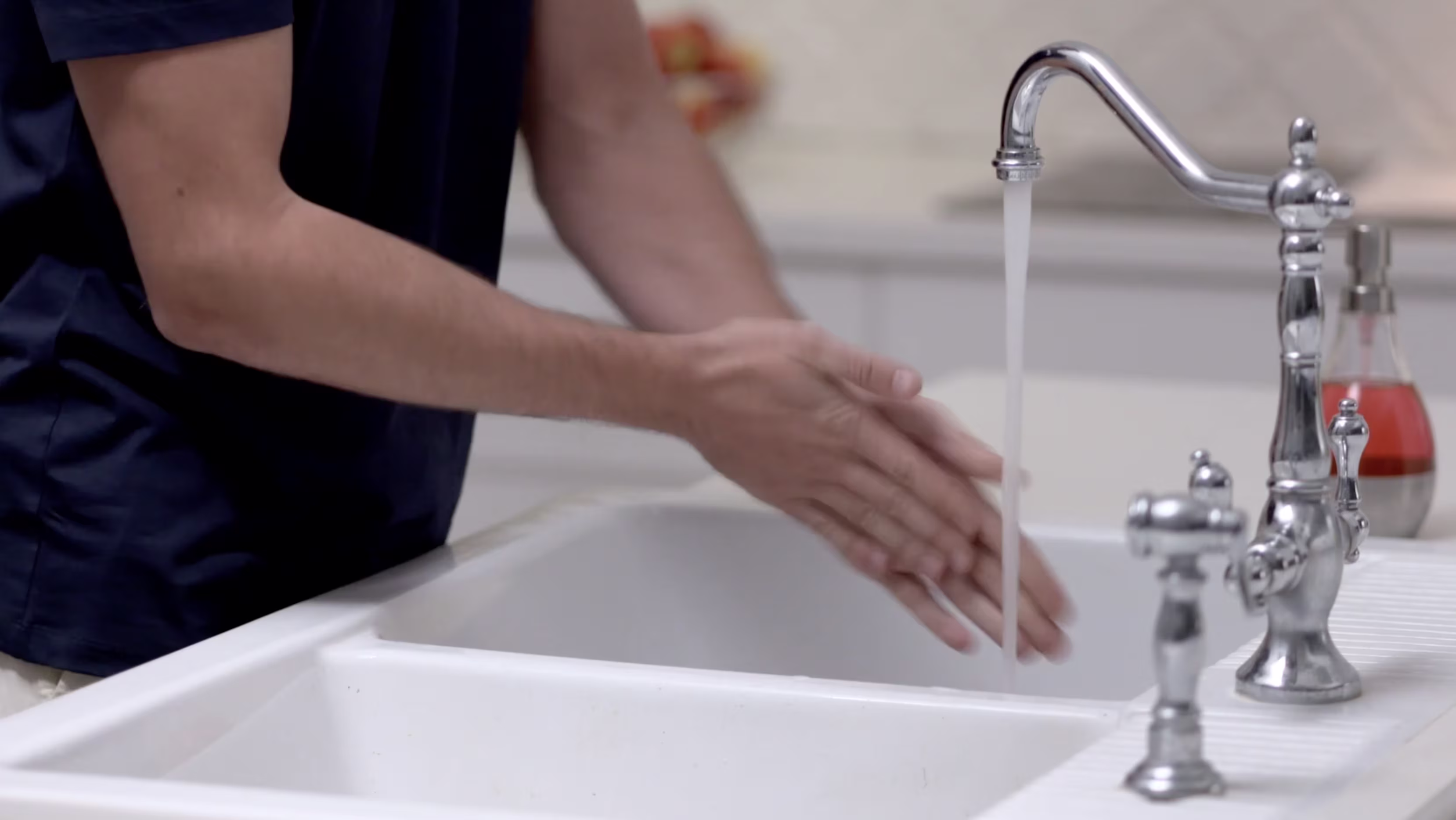 Person washing their hands under running water at a sink as part of a hygiene step before a procedure.